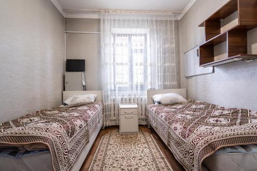 two beds in a small room with a window at Half,Гостевой дом in Karakol