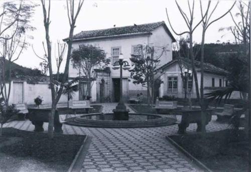 uma foto a preto e branco de uma casa com uma fonte em Casa Centenária localizada no calçadão de SLP em São Luiz do Paraitinga