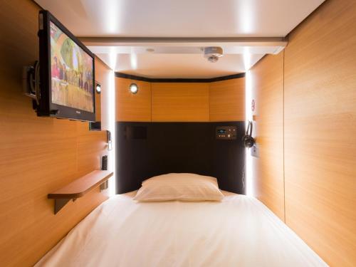 a bedroom with a bed with a tv on the wall at Sauna & Capsule Hotel Rumor Plaza in Kyoto