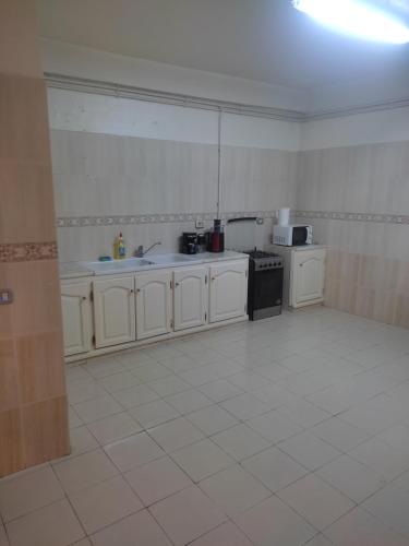 a kitchen with white cabinets and a white tile floor at Appart Cozy in Le Bardo