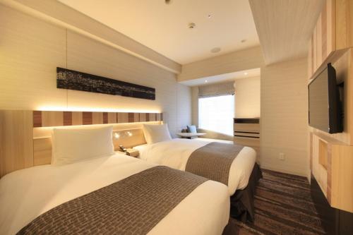 a hotel room with two beds and a flat screen tv at Hotel Sunroute Ginza in Tokyo