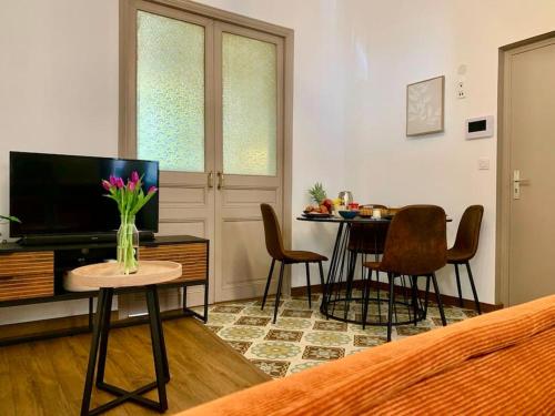 uma sala de estar com televisão e uma mesa com cadeiras em L'Ambre - Appartement Raffiné em Perpignan