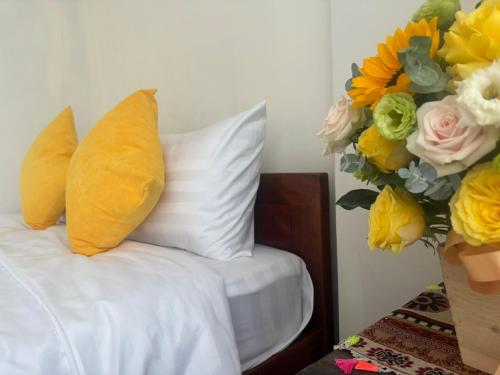 a bed with yellow pillows and a bouquet of flowers at Good Morning Hoi An Homestay and Hostel in Hoi An