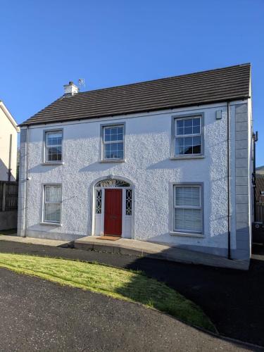 a white house with a red door on a street at Ballapousta in Ballycastle