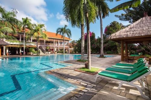 uma piscina num resort com espreguiçadeiras e palmeiras em Plagoo Holiday Hotel em Nusa Dua