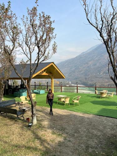a woman walking through a park with tables and chairs at Regenta Inn by Riverside Manali in Manāli