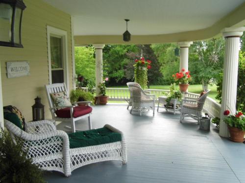 un porche con sillas blancas de mimbre y un cojín verde en Finger Lakes Wine Trail "Heart" Garden Suite, en Interlaken