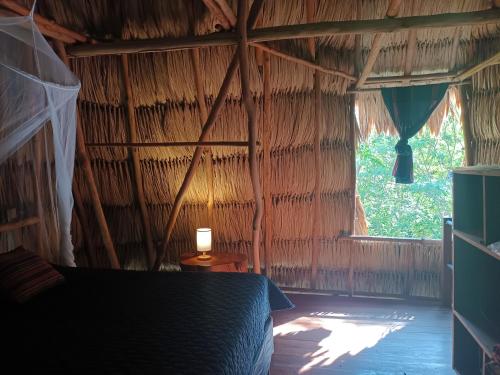 a bed in a thatched room with a window at Alice Guesthouse in El Remate