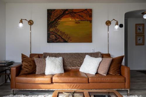 a living room with a brown leather couch with pillows at Elk Rapids Bungalow Garden Firepit AC in Elk Rapids