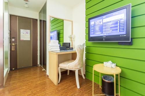 a room with a green wall with a desk and a tv at Newrise Hotel in Kaohsiung