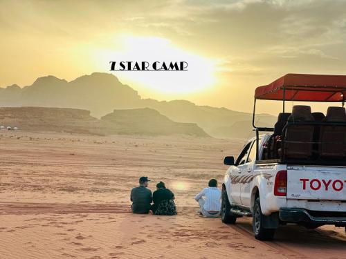 a group of people sitting in the sand near a truck at 7star camp in Wadi Rum