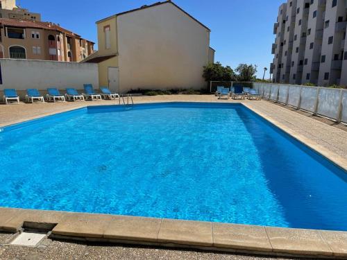 une grande piscine bleue avec des chaises et un bâtiment dans l'établissement Le Bleu Soleil de Barcarès, au Barcarès