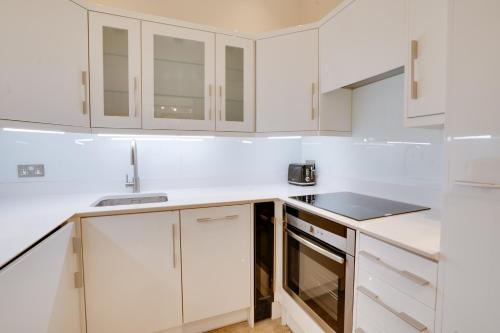 a white kitchen with white cabinets and a sink at Designer Retreat by Green Park in London