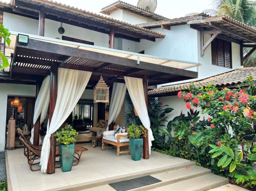 een patio van een huis met gordijnen en bloemen bij Casa Sonho da praia beira-mar 04 suítes in Barra de Santo Antônio