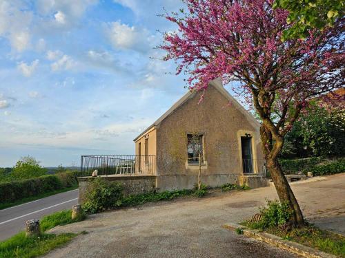 un pequeño edificio con un árbol florido al lado de una carretera en Gite au pied de la Colline en Vézelay