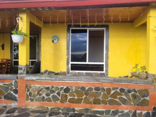 a yellow house with a window and a stone wall at Alojamiento EL GITANO in Filandia