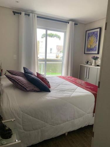 1 dormitorio con cama con almohadas y ventana en Sobrado Charmoso e Aconchegante / Santa Felicidade PR en Curitiba