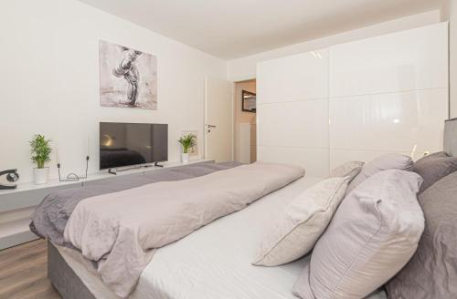 a white bedroom with a large bed and a tv at Apartman Holiday in Šibenik