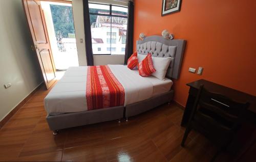 a bedroom with a bed with orange walls and a window at Hotel Horizonte in Machu Picchu