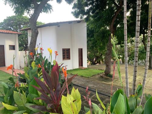 un bâtiment blanc avec des arbres et des fleurs dans une cour dans l'établissement Morro Branco Suítes - Hospedaria Morro Branco, à Beberibe