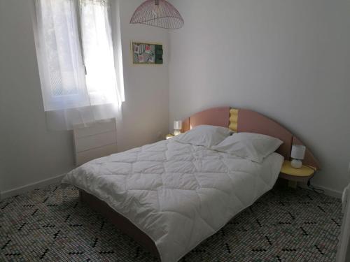 a bedroom with a white bed with a wooden headboard at Logement Soulac-sur-mer 4 personnes in Soulac-sur-Mer