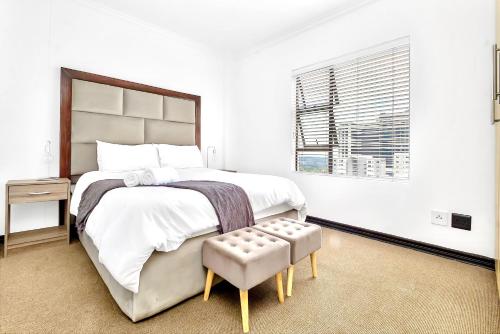 a white bedroom with a large bed and a window at Sandton Lux, CBD, 2 Bedroom & 2 Ensuite, No Load shedding in Johannesburg