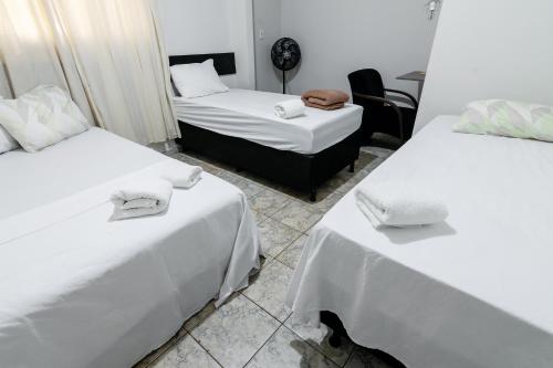 a room with two beds with white sheets at Quarto 05 Pousada Roosevelt in Uberlândia