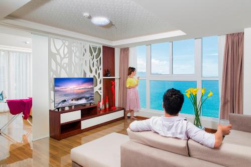 a man sitting on a couch in a living room watching a woman at Paris Luxury Hotel & Apartment Nha Trang in Nha Trang