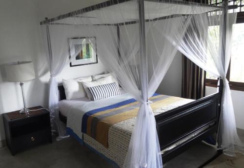 1 dormitorio con cama con dosel y cortinas blancas en Monkey manor villa, Strathisla Tea Estate Bungalow en Matale