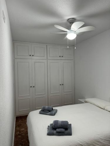 een witte slaapkamer met een plafondventilator en 2 handdoeken op een bed bij Playa Villajoyosa, apartamento in Villajoyosa