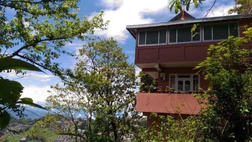a red house with a balcony and trees at Travellers' Den in Darjeeling