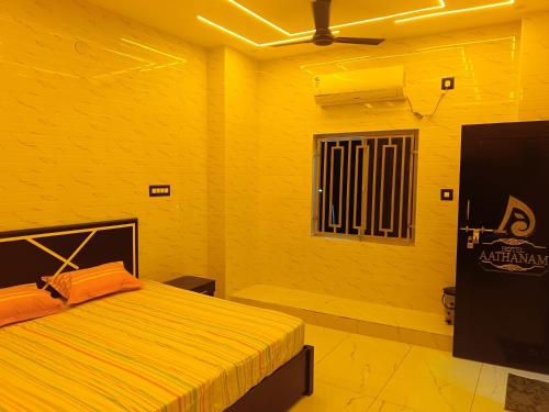 a yellow room with a bed and a television at Aathanam in Kanyakumari