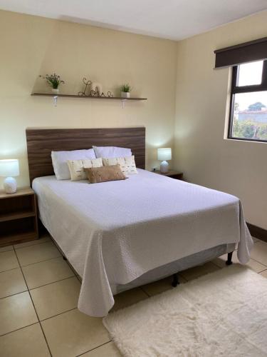 - une chambre dotée d'un grand lit avec des draps blancs et une fenêtre dans l'établissement Mi casa es tu casa., à Quetzaltenango