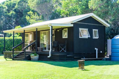 una piccola casa nera con un portico sull'erba di The Cabin - Mangawhai Heads Studio a Kaiwaka