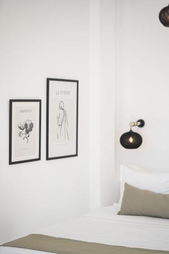 two framed prints on a white wall next to a bed at La Roka, Cliffside Memories in Imerovigli