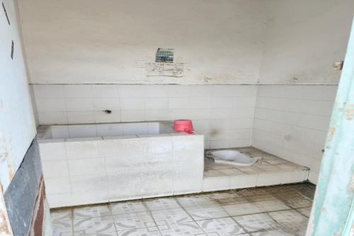 a white tiled bathroom with a toilet in it at SPOT ON 93894 Jamil Homestay Syariah in Plosobegem