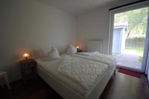 uma cama branca num quarto com uma grande janela em K 94 - Stilvolles Ferienhaus mit Kamin in Roebel an der Mueritz em Marienfelde