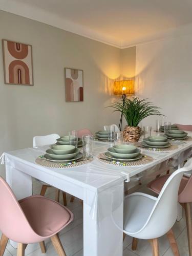 - une table à manger blanche avec des assiettes et des chaises vertes dans l'établissement Maison chaleureuse 4 chambres avec jardin - Proche Paris - ARENA Paris Nord Villepinte - Parc des expositions - Aéroport CDG - Disney - Astérix, à Tremblay-en-France