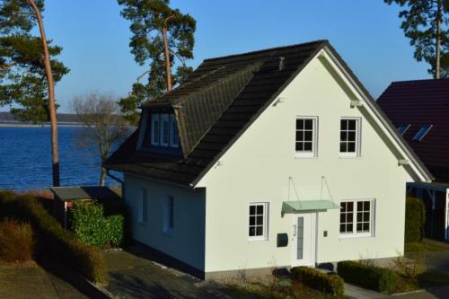 una casa blanca con un techo negro junto al agua en 7 OG - Charmante Ferienwohnung mit traumhaften Seeblick und Balkon in Röbel an der Müritz, en Marienfelde