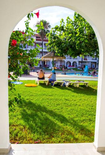 an archway with people sitting in the grass near a pool at Apartments Kione Playa Romana Park in Alcossebre