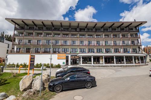 ein Gebäude mit zwei davor geparkt in der Unterkunft Hotel Toliar in Štrbské Pleso