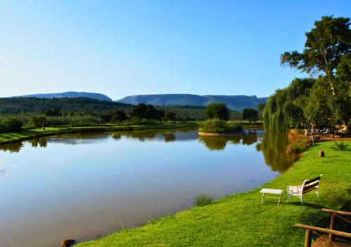 two benches sitting on the grass next to a river at Imbabali Retreat & Venue in Magaliesburg