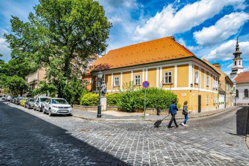 zwei Menschen, die eine Kopfsteinpflasterstraße entlang laufen, in der Nähe eines gelben Gebäudes in der Unterkunft Academy Pension in Budapest