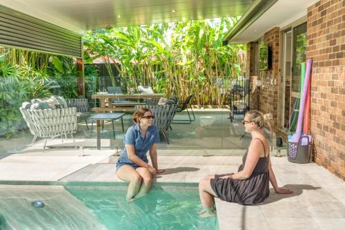 two women sitting in a swimming pool at Sandy Dunes Retreat Pet-Friendly Wurtulla Home in Kawana Waters