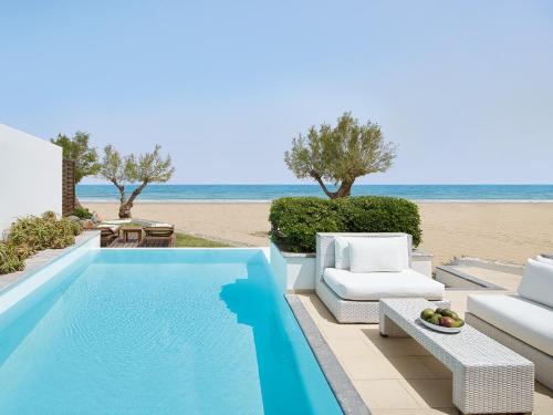a swimming pool next to a beach with two chairs at Amirandes, A Grecotel Resort to Live in Gouves