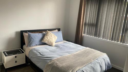 a bedroom with a bed with blue pillows and a window at Comfy & Sunny home in Wellington in Wellington