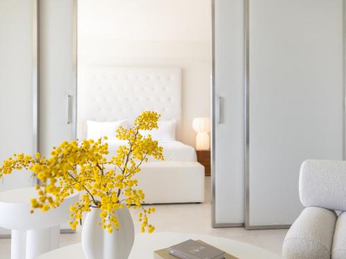a white room with a white bed and a vase with yellow flowers at Amirandes, A Grecotel Resort to Live in Gouves