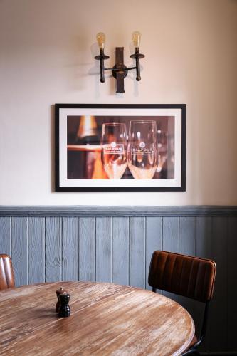 a table with two wine glasses and a picture on the wall at The Swan at Forest Row in Forest Row