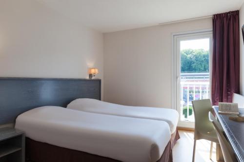 two beds in a hotel room with a window at The Originals City, Hôtel Le Louisiane, Belfort Sud (Inter-Hotel) in Andelnans