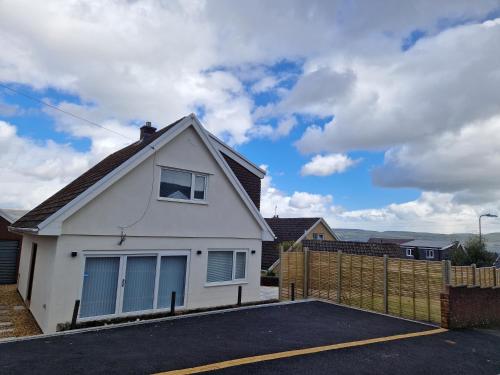 a white house with a fence in a parking lot at Modern Detached 3 bedroom home with off-road parking & bike store in Abercanaid